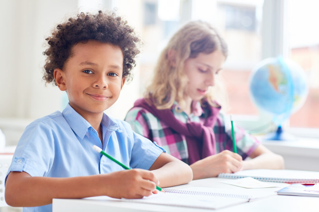 menino sorrindo enquanto escreve com lápis no caderno para representar blogposts sobre estratégias para retenção de alunos
