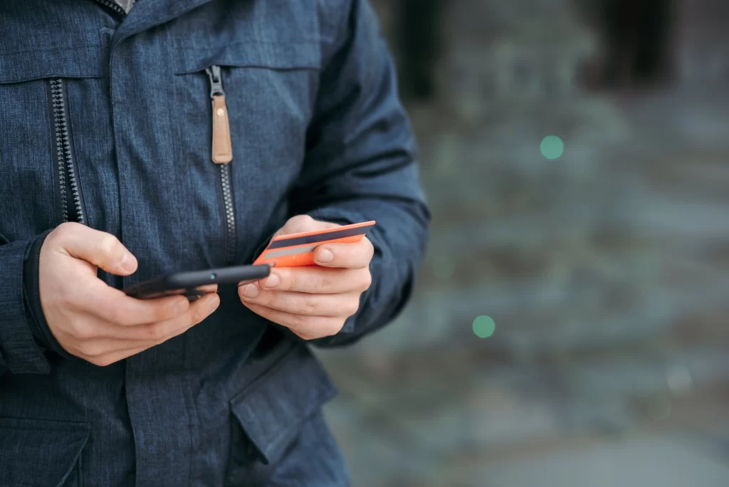 homem segurando celular e cartão nas mãos para ilustrar blogpost sobre sistema de cobrança de mensalidade escolar
